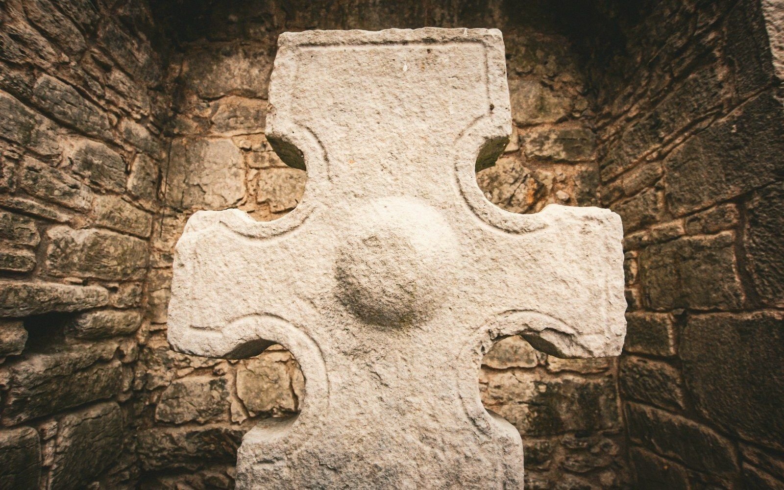 Weathered stone Celtic cross with a carved boss, set against a rough masonry wall