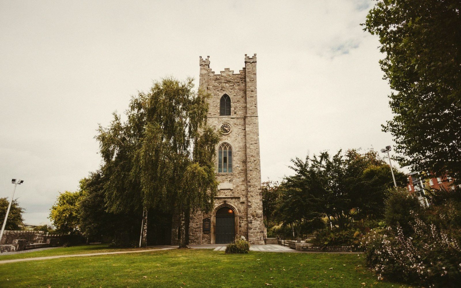 Stone church tower with an arched doorway stands amid trees and a grassy lawn